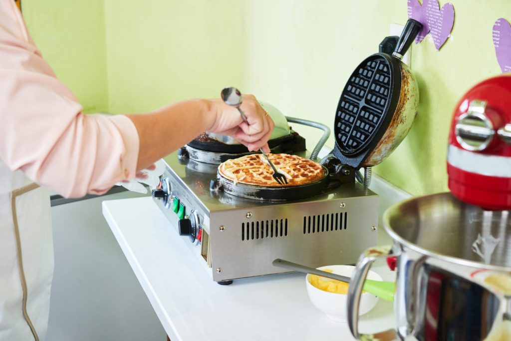 señora sacando el waffle cocinado de una wafflera