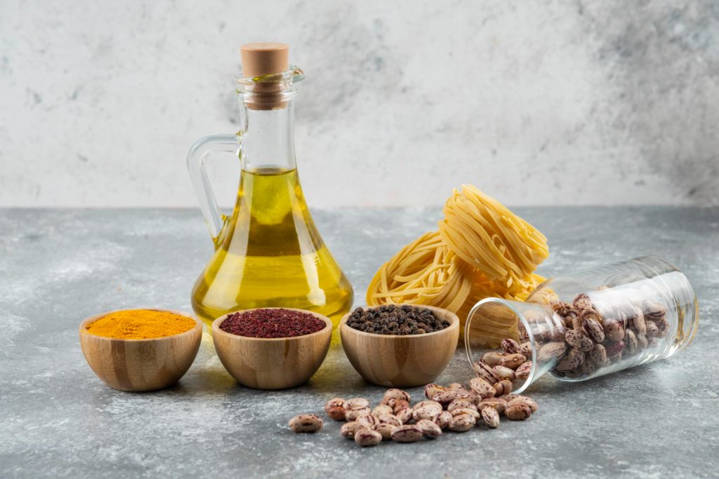 Frasco de aceite de oliva con frutos secos al rededor en platos