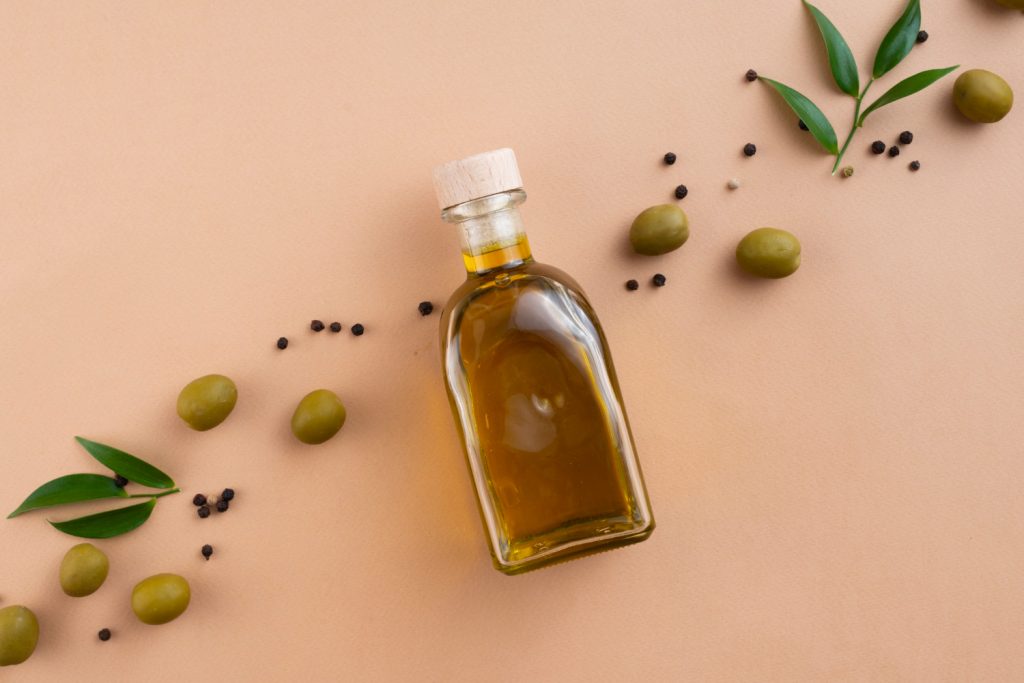 Frasco de aceite de oliva sobre mesa rosada con semillas al rededor