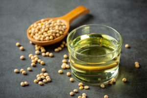 Semillas de soja sobre una cucharada de madera al lado izquierdo de un pequeño frasco con aceite
