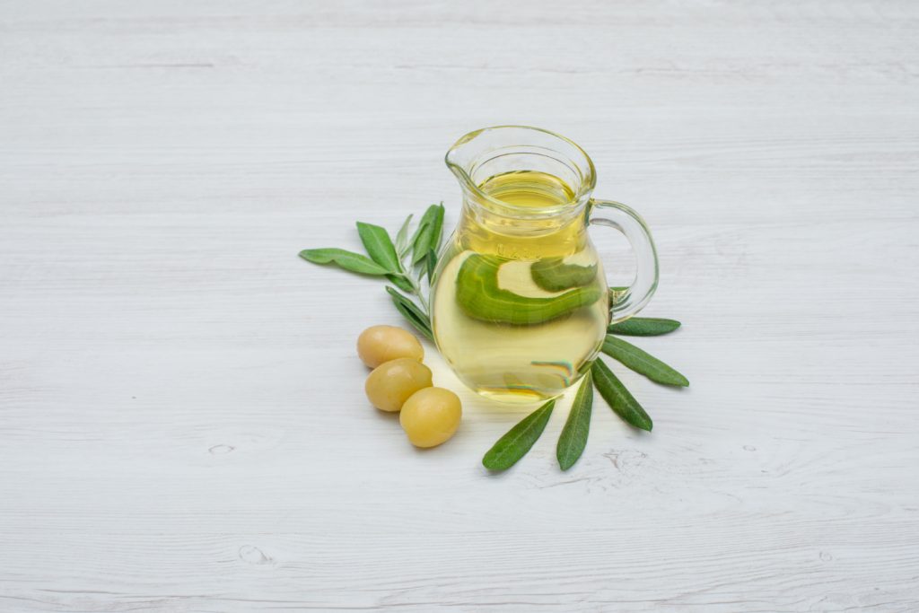 frasco pequeño de aceite de oliva con hojas y semillas al rededor